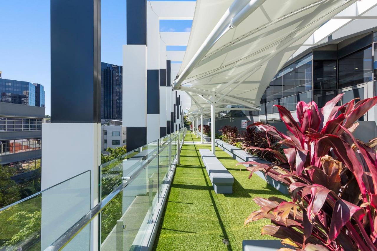 Meriton Suites Herschel Street, Brisbane Exterior foto The photo shows a modern outdoor terrace or balcony area featuring a green lawn-like surface. There are multiple planters with vibrant plants, adding a touch of color. The space has a sleek, contemporary design, with large glass panels providing safe