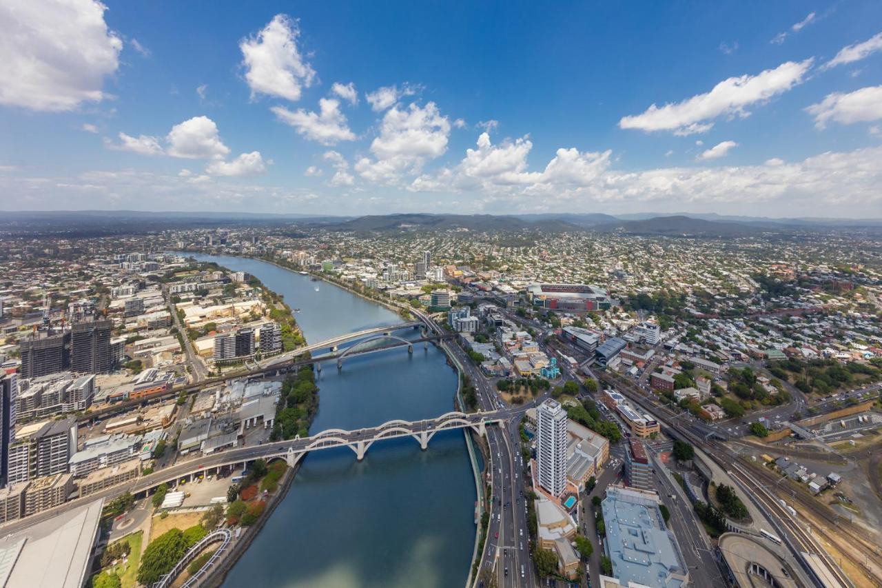 Meriton Suites Herschel Street, Brisbane Exterior foto The photo shows an aerial view of an urban landscape featuring a river winding through the city. There are several bridges crossing the river, which appears to be fairly wide. The surrounding area is densely populated with buildings, both residential