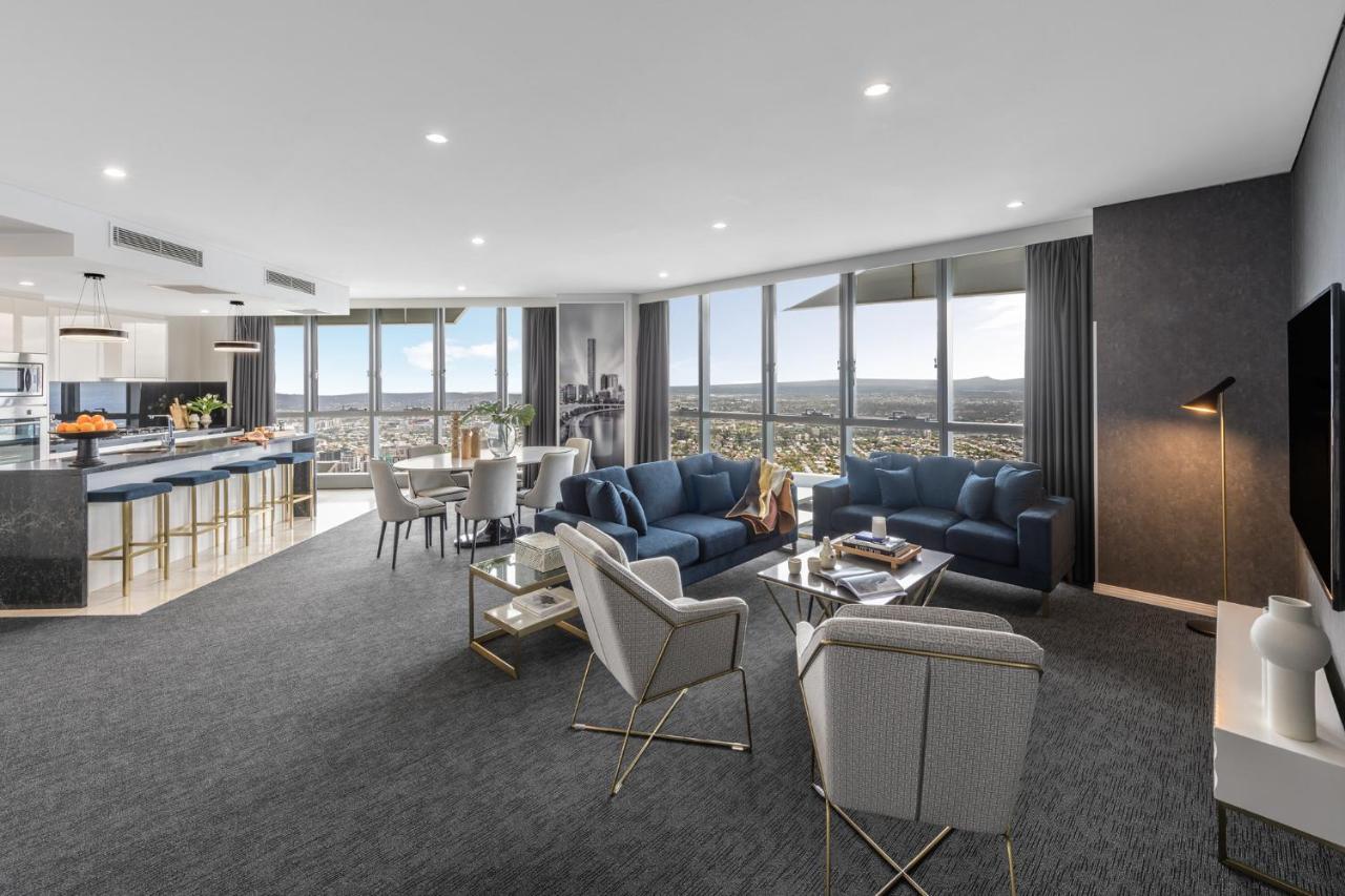 Meriton Suites Herschel Street, Brisbane Exterior foto The photo depicts a modern and stylish living area within a high-rise apartment. The space features large windows that offer a panoramic view of the cityscape. 

1. **Seating Area**: There are two blue sofas and several light-colored chairs arranged 