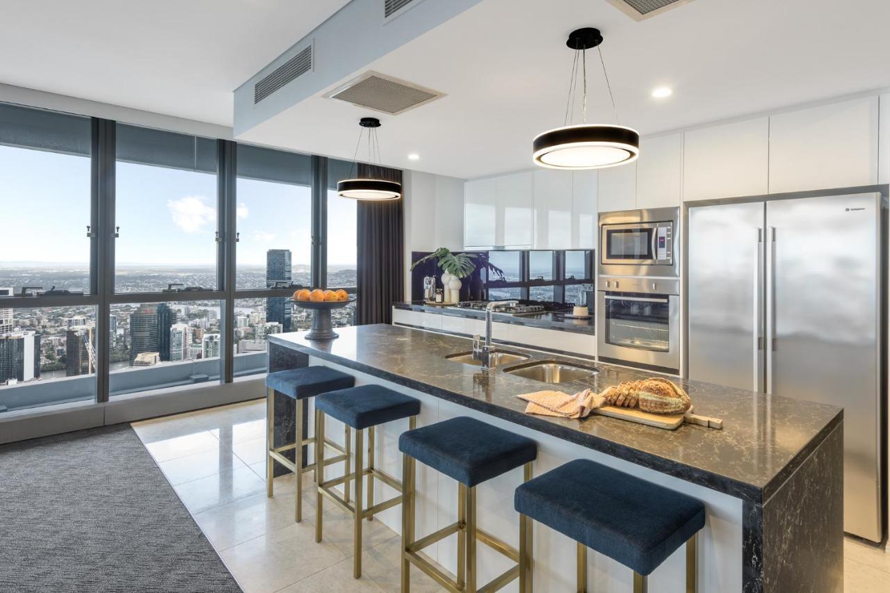 Meriton Suites Herschel Street, Brisbane Exterior foto The photo shows a modern kitchen with a spacious and sleek design. It features a large island with a dark countertop and several bar stools with blue upholstery around it. There are built-in appliances, including an oven and a refrigerator, integrate