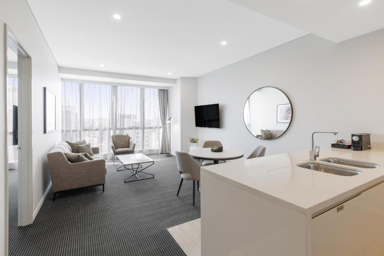 Meriton Suites Herschel Street, Brisbane Exterior foto The photo shows a modern, well-lit living space that appears to be a hotel room or an apartment. It features a cozy seating area with two armchairs and a small coffee table, along with a larger dining table with chairs. There is a round mirror on one