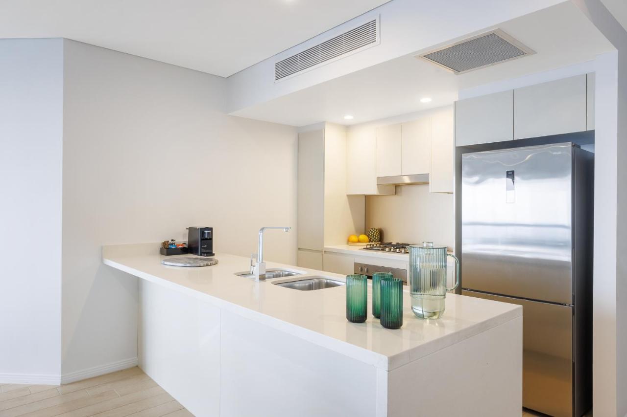 Meriton Suites Herschel Street, Brisbane Exterior foto The photo depicts a modern kitchen with a clean and minimalist design. It features a white countertop that extends into a bar area. Behind the counter, there is a sink and possibly a stovetop. The cabinetry is light-colored, contributing to the airy 
